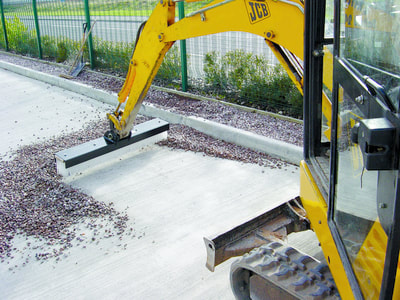 Side view of mini digger using Boom Broom sweeper attachment.